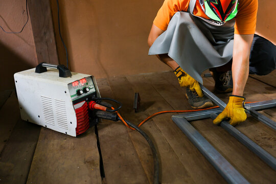 Skilled welder using welding machine to join metal frame parts in workshop with protective equipment and sparks absent