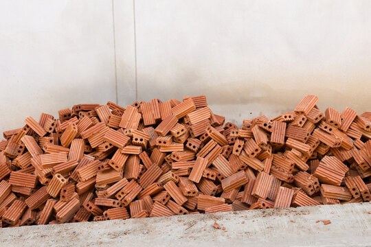 Terracotta ceramic brick pieces piled against pale wall, showing hollow channels, ribbed surfaces, rough texture, and scattered construction material in warm earthy tones for building use