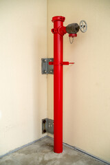 A red metal fire hydrant pipe stands in the corner of a light building wall. © AncientAftertone