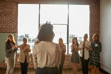 Fototapeta premium Group applauding a speaker in a sunlit brick-walled room.