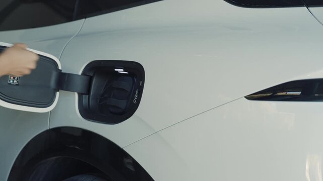 Person plugging in EV charging cable to white electric vehicle for sustainable energy transport.