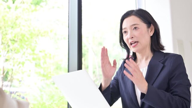 笑顔で説明する50代の日本人女性ビジネスパーソン、住宅のローン金利見直しのファイナンシャルプランナや、顧客との商談や提案、面談でコミュニケーションする管理職のイメージの動画