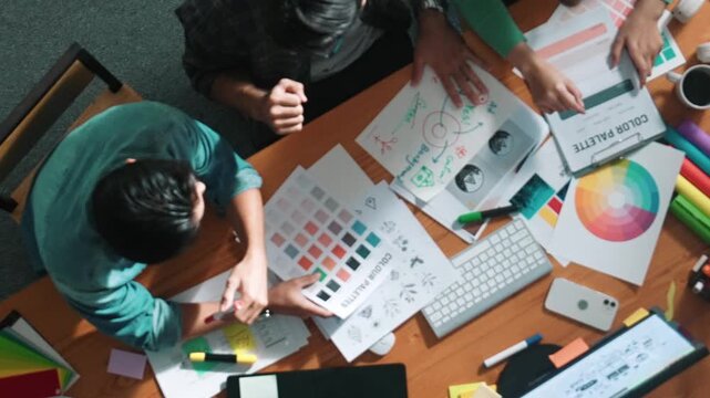 Top down aerial view of project manager looking at screen while designer writing idea. Smart business team explain idea of logo design while designer choose theme while looking at palette. Symposium.