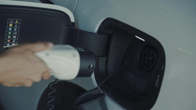 Person plugging in EV charging cable to white electric vehicle for sustainable energy transport.