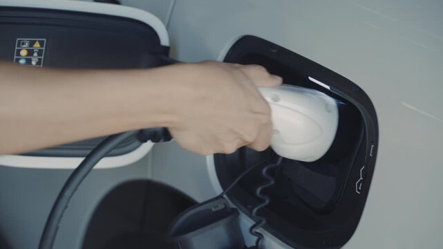 Person plugging off EV charging cable to white electric vehicle for sustainable energy transport.