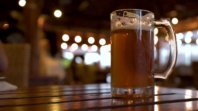 Two cold beer mugs on wooden table with blurred background lights and movement.
