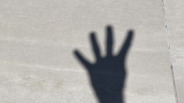 Hand gestures counting from zero to five on sunny day shadow on paved ground footage.