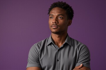 Fototapeta premium A man in a gray short-sleeved button-down shirt poses with arms crossed against a solid purple background.