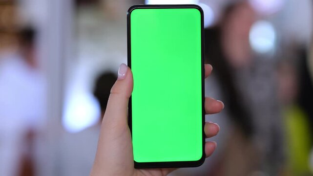 Hand holds smartphone with green screen. Background blurred with people. Three keyframes show same scene. Phone screen fully green. Hand appears steady in each frame