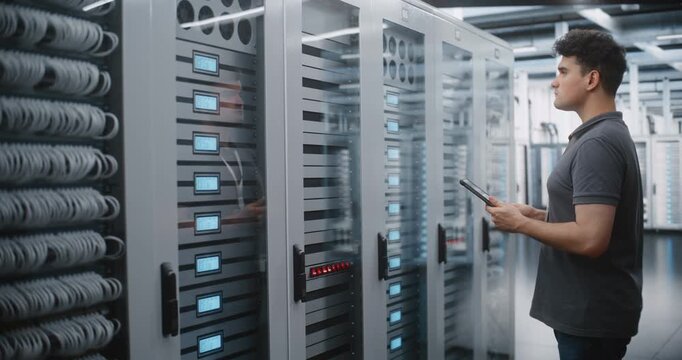 Male Data Center Engineer Audits Server Racks with Tablet, Checking Equipment Indicators and Cable Organization While Verifying Infrastructure During Mobile Inventory and Technical Maintenance Rounds.