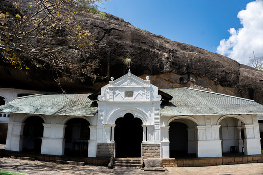 White arch entrance and colonnade of cave temple built beneath huge rock face at Dambulla