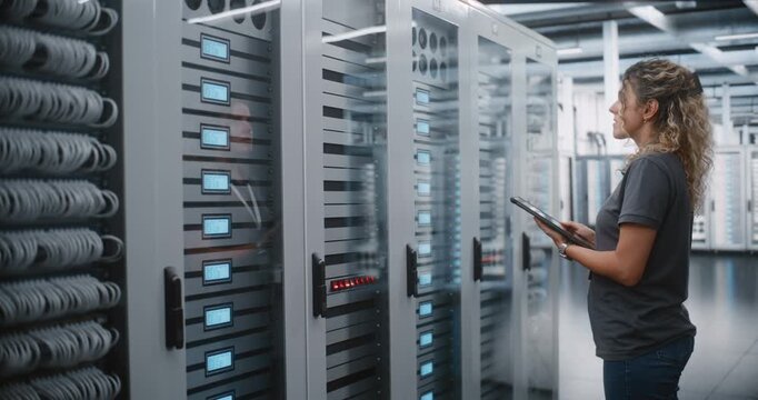 Female Data Center Engineer Uses Tablet to Inspect Server Rack Indicators and Patch Cable Routing, Performing Mobile Equipment Inventory and Physical Infrastructure Audit During on site Maintenance.