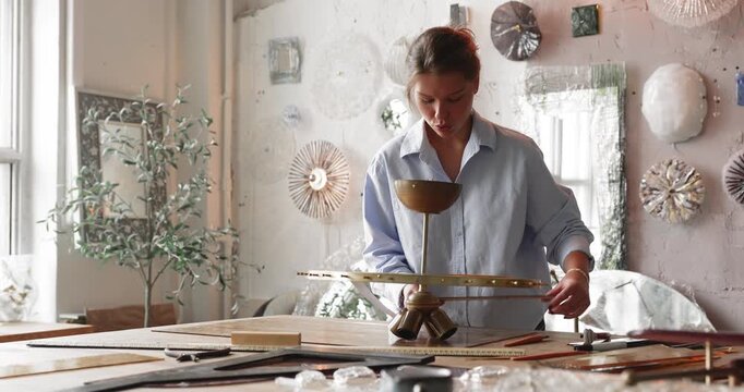 Young woman glass workshop specialist measuring proportions of metal lamp frame planning decorative composition analyzing dimensions and preparing design scheme before installing glasswork components