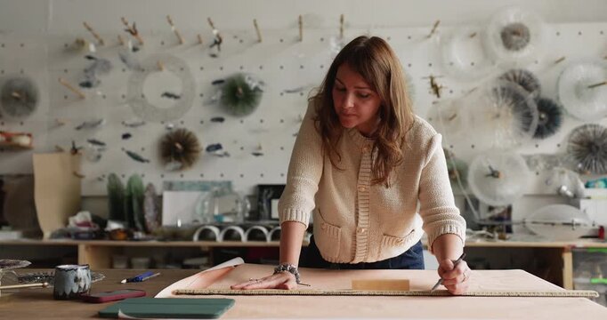 Busy older adult craftswoman making blueprint on paper sheet developing technical sketch for glass project creating architectural drawings by hand with ruler and pencil at table in workshop studio