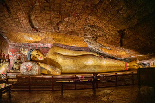 Large golden reclining Buddha statue under painted rock ceiling in Dambulla Cave Temple