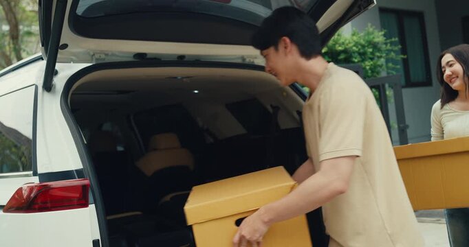 Young Asian couple carries cardboard boxes to load car trunk while moving out. Family relocation home mortgage loan, Real estate moving transport vehicle, New house package delivery pack concept.