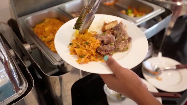 Food service worker plating beef stir fry with noodles in restaurant buffet line
