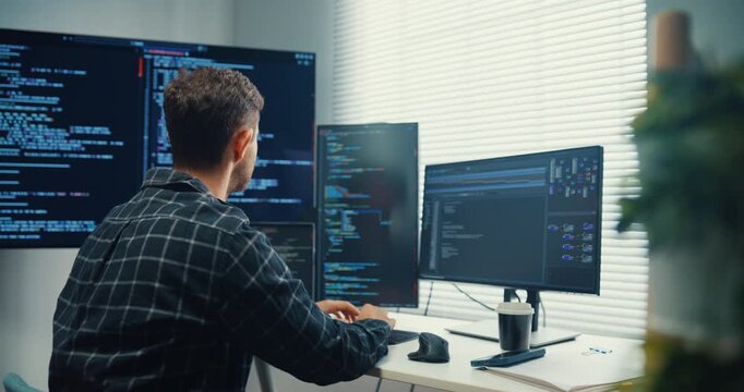 Young Caucasian male programmer writes code using multiple screens in home office workspace. AI development, cybersecurity, network database system, software engineering, remote tech startup concept.