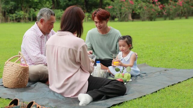 Happy Asian family having fun time on picnic at city nature park sunny day, outdoor activitie with daughter father, mother and grandfather