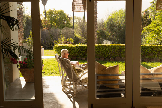 profile of elderly man relaxing in chair at sunset framed through windows