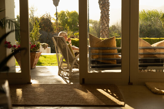 profile of elderly man relaxing in chair at sunset framed through windows
