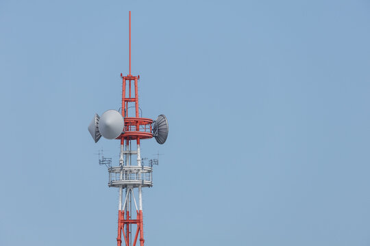 Upper section of a red-and-white communication tower featuring parabolic dish antennas, stacked circular ring platforms, directional Yagi arrays, and dipole antennas against a clear blue sky.
