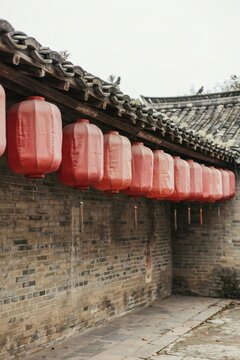 Row of plain red silk lanterns hung from a courtyard eave above a grey brick wall