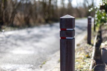 Wooden post stands beside quiet country road. Red stripes mark its top, simple and bold. Sunlight glints off gravel, soft and warm. Background trees blur, nature feels calm. Ideal for themes of trails © Alexandr