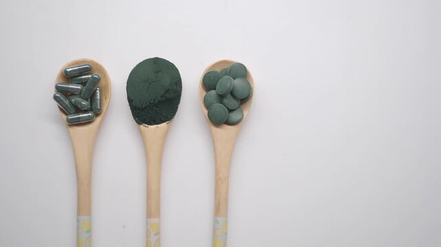 Spirulina supplements in various forms displayed on wooden spoons over white background in top down motion clip