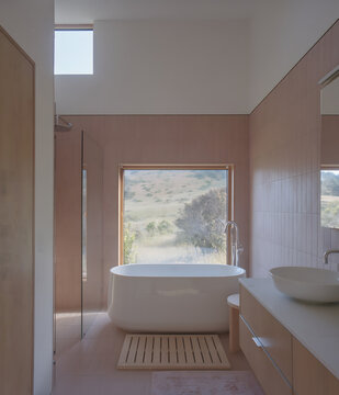 Modern minimalist bathroom interior with a freestanding white bathtub and a large window overlooking a scenic natural landscape view