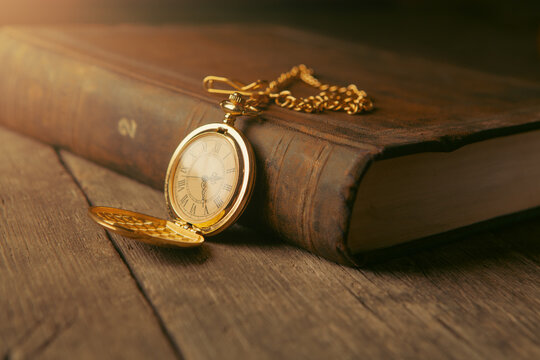 pocket watch on old book on wooden background, closeup