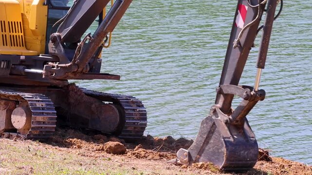 Excavator digging earth near water body construction site heavy machinery working.