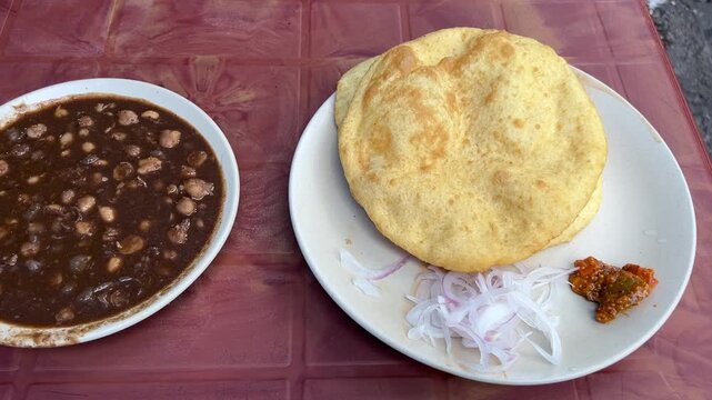 Spicy chana masala with bhatura prepared in Punjabi style in Kolkata; professional food photography of authentic Punjabi chole bhature, puffed deep fried bread, dark spiced chickpea curry, Kolkata str