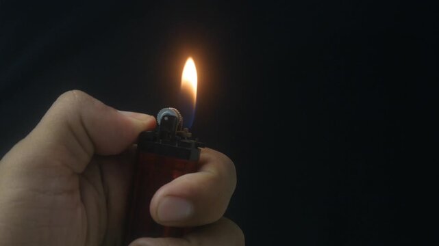 Hand holding a burning gas lighter with a small flame on a dark background