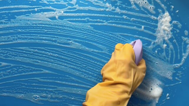 Scrubbing a Foamy Blue Surface with a Brush and Yellow Gloves