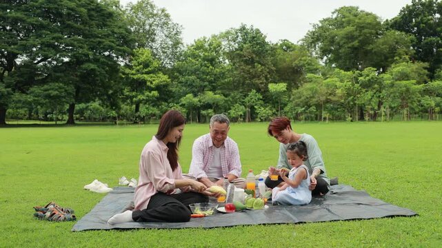 Happy Asian family having fun time on picnic at city nature park sunny day, outdoor activitie with daughter father, mother and grandfather