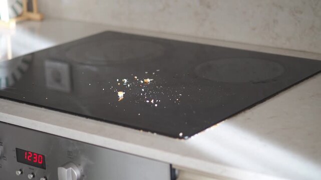 Sunlight rays streaming into kitchen through window illuminating dirty induction hob with crumbs slow motion close up