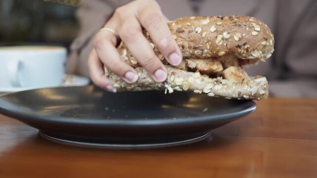 Woman picking up a freshly baked multigrain chicken sandwich from plate, close-up dynamic indoor shot
