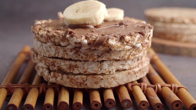 Stack of puffed rice cakes topped with chocolate hazelnut spread and fresh banana slices on bamboo mat