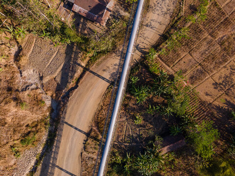 Aerial View of a Covered Conveyor Belt System with Checkpoint Buildings and a Service Road Crossing Hilly Terrain Near a Residential Area in Indonesia