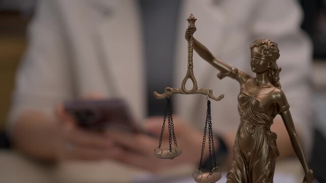 Lady Justice Statue with Legal Professional Using Smartphone in Law Office