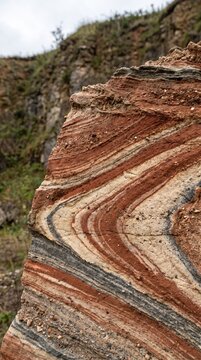 Jagged sedimentary rock formation featuring distinct wavy colorful mineral strata layers under soft natural daylight conditions