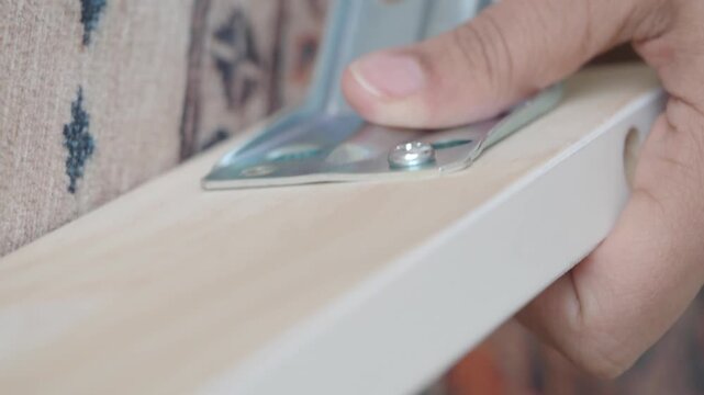 Close up of hands using an electric screwdriver to attach metal bracket to wood