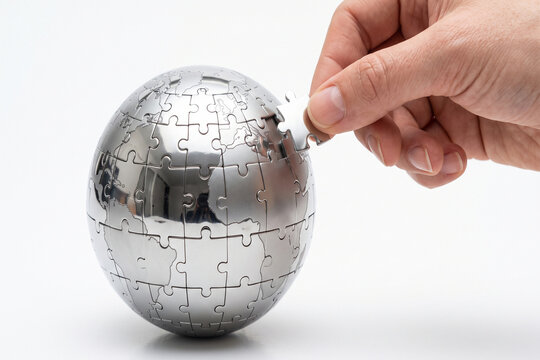 Hand placing last puzzle piece onto metallic globe against white background for global connectivity concept