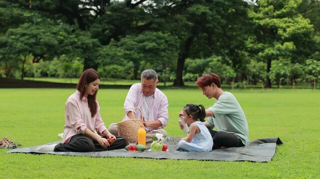 Happy Asian family having fun time on picnic at city nature park sunny day, outdoor activitie with daughter father, mother and grandfather