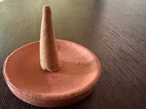eco-friendly Indian dhoop cone made from organic cow dung, placed on a terracotta clay holder over a textured wooden background. Ideal for spiritual rituals, meditation, and wellness concepts.