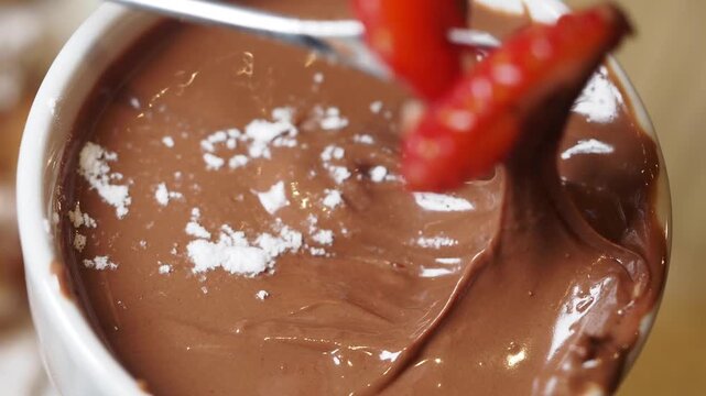 A close up cinematic shot of a fresh red strawberry being dipped into a delicious bowl of creamy melted chocolate fondue, perfect dessert footage