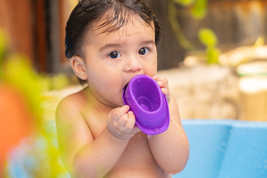 Baby with wet hair playing with a purple cup during bath time. Infant portrait of water play, hygiene, sensory exploration and everyday routine.