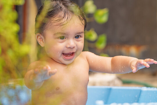 Smiling baby with wet hair enjoying bath time in a blue tub. Joyful scene of water play, infant hygiene, wellness and everyday care.