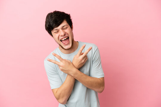 Young Russian man isolated on pink background smiling and showing victory sign